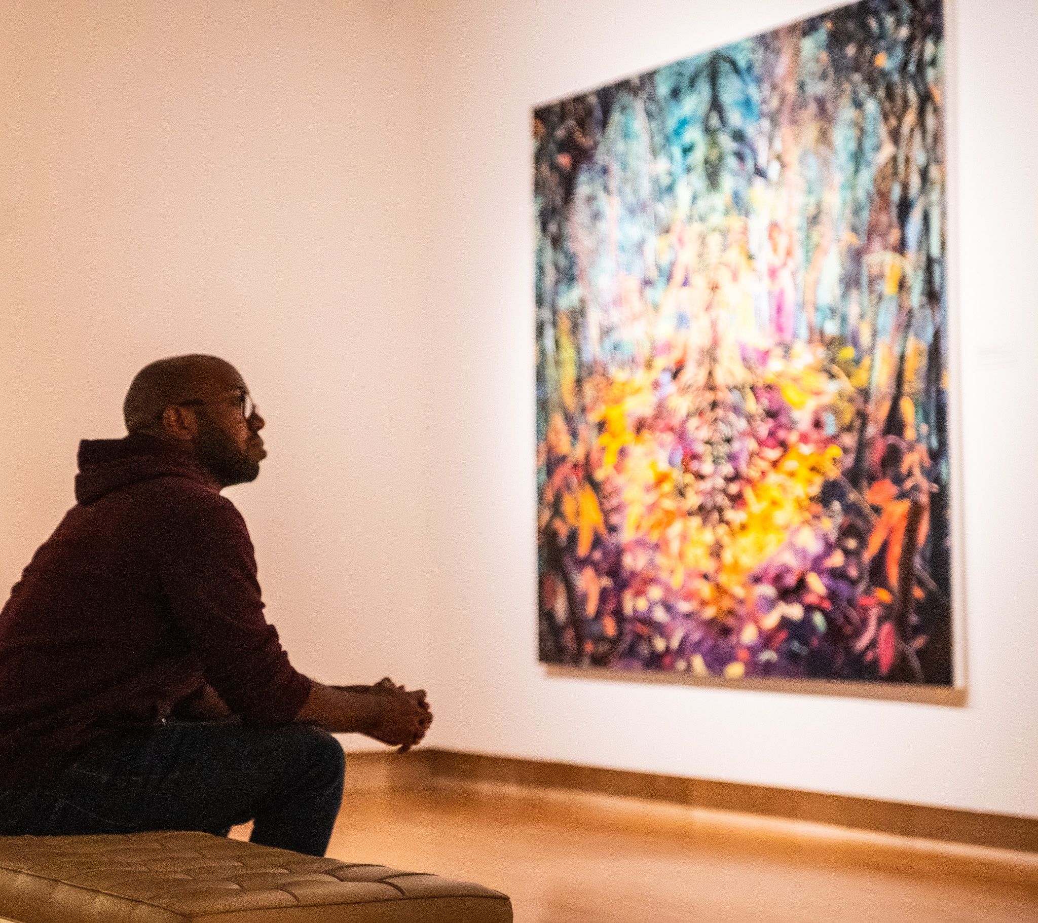 Visitor seated in a gallery looking at a colorful abstract painting.
