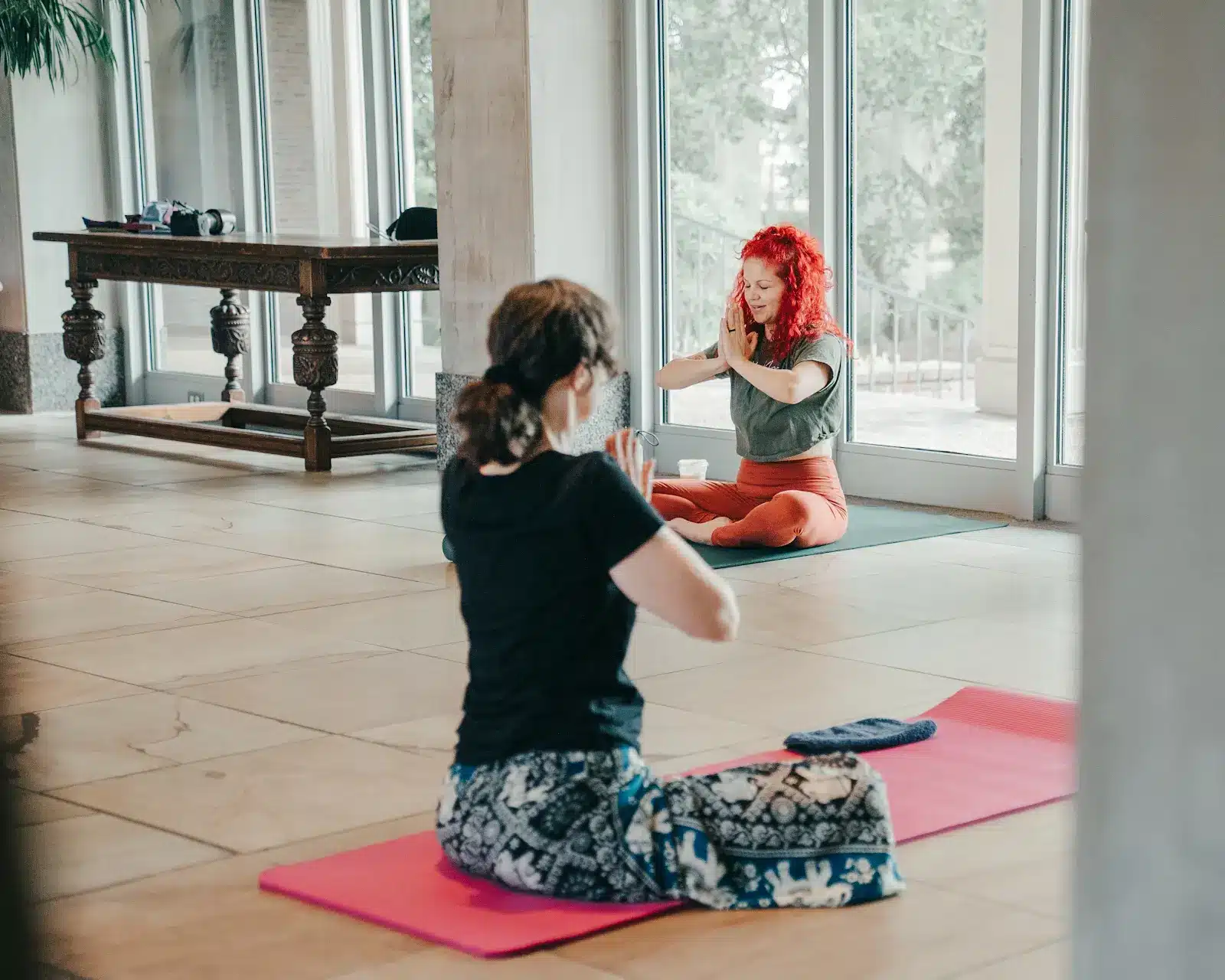 Yoga participants seated on mats with hands together in a light-filled museum space.